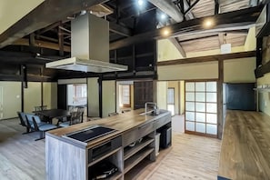 A spacious kitchen with a large island, wooden flooring, and a high ceiling with exposed beams. - Takeda Base Inn (Asago)
