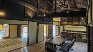 A spacious room with a high ceiling, wooden beams, a dining area with a long table and chairs, and a kitchen area with a counter and stools. - Takeda Base Inn (Asago)
