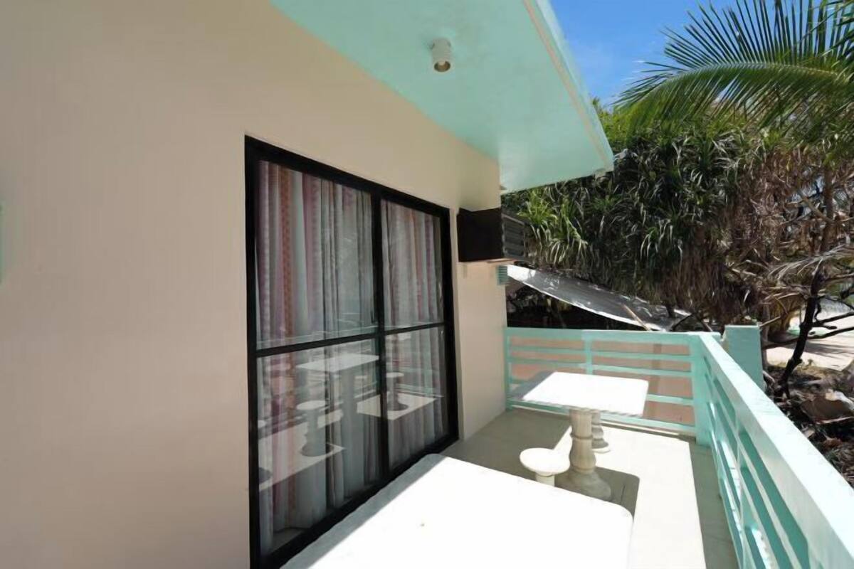 A balcony with a table and chairs, a window with curtains, and a view of palm trees.