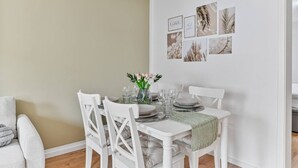 A dining area with a white table set for four, surrounded by white chairs. There is a vase with flowers on the table, and a wall with framed pictures above it. - Work & Stay - Apartment with office (Leinfelden-Echterdingen)