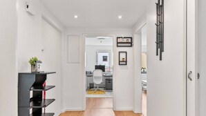 A hallway leading to a room with a desk and chair, a shelf with items, and a door with a number sign. - Work & Stay - Apartment with office (Leinfelden-Echterdingen)