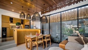 Une cuisine moderne avec des meubles en bois, un coin repas comprenant une table et des chaises en bois, et une grande fenêtre donnant sur un paysage verdoyant.