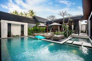 Un espace piscine moderne, doté de chaises longues et de parasols, entouré de plantes tropicales et surplombé d’un ciel dégagé.