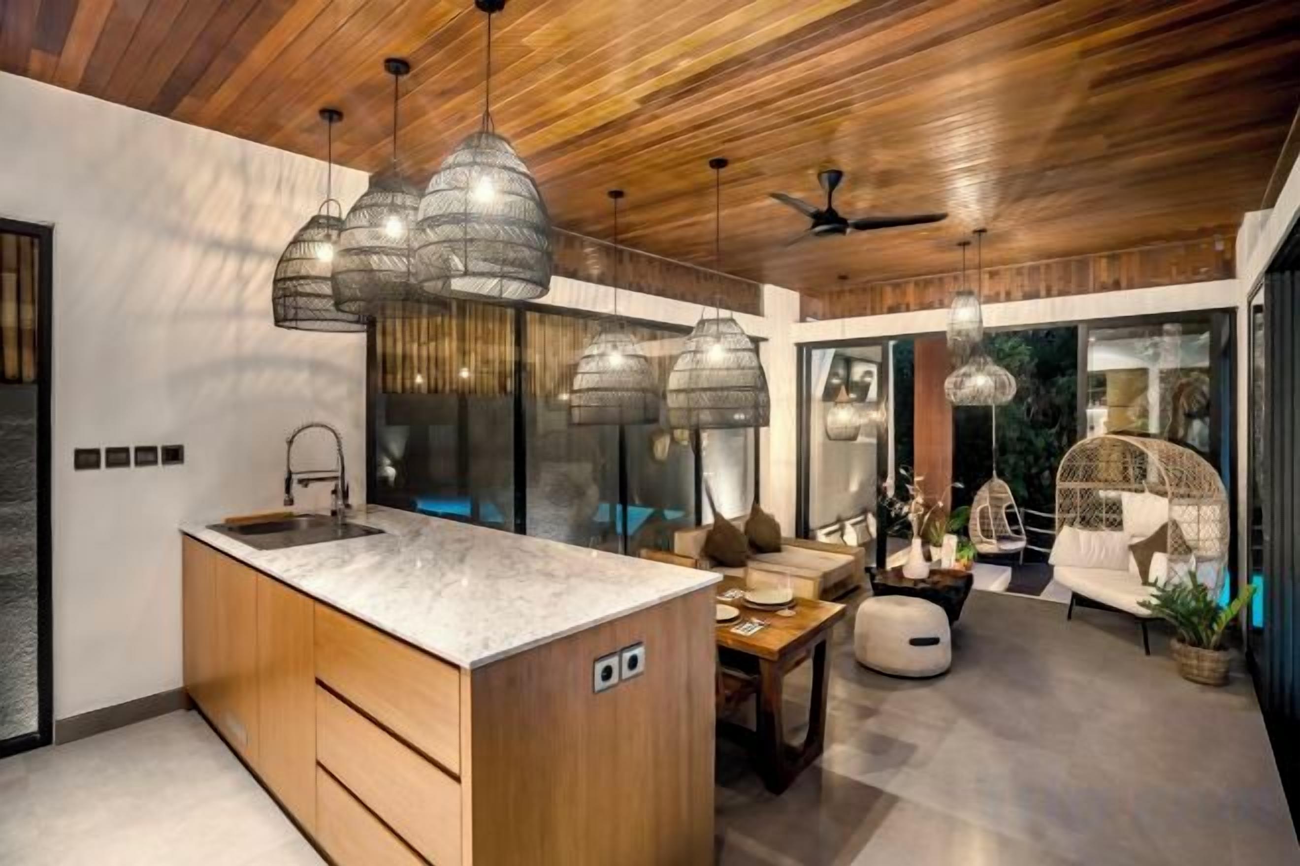 A modern kitchen with a large island, pendant lighting, and a dining area with a sofa and table.