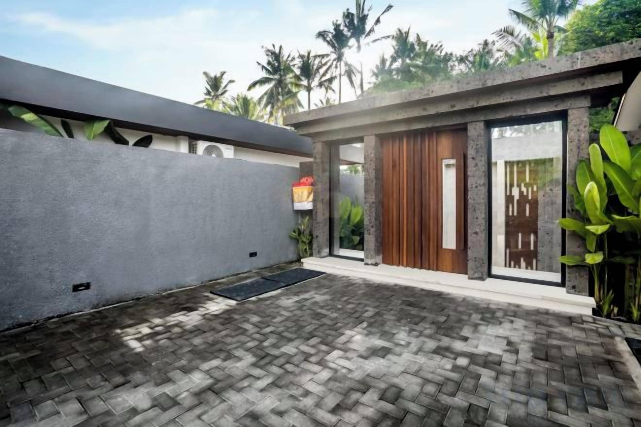 A modern house with a paved courtyard, a wooden door, and a concrete wall.
