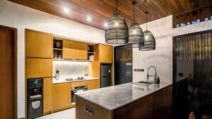 Une cuisine moderne avec des meubles en bois, un plan de travail en marbre et des luminaires suspendus.