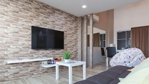A modern living room with a stone wall, a flat-screen TV, a sofa, a small table with a plant, and a window with curtains. - 3-Bed Exec Suite RumahKu Airport Penang (Bayan Lepas)