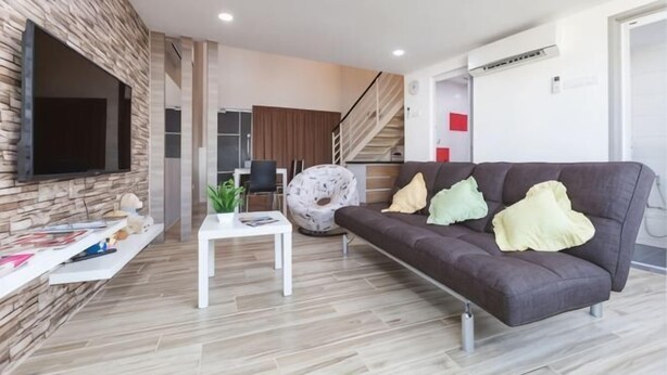 A modern living room with a flat-screen TV, a sofa with cushions, a coffee table, and a staircase leading to another level. - 3-Bed Exec Suite RumahKu Airport Penang (Bayan Lepas)