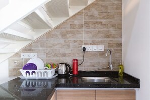 A kitchen with a black countertop, a sink, a red kettle, and a dish rack with plates.