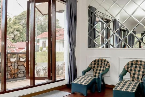 A room with a large window, a stone wall, and two chairs with checkered covers. - Sierra by Semusim Villa (Cipanas)