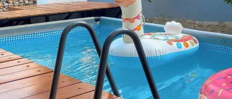 A swimming pool with a wooden deck, a llama-shaped inflatable float, and a pink donut-shaped float.