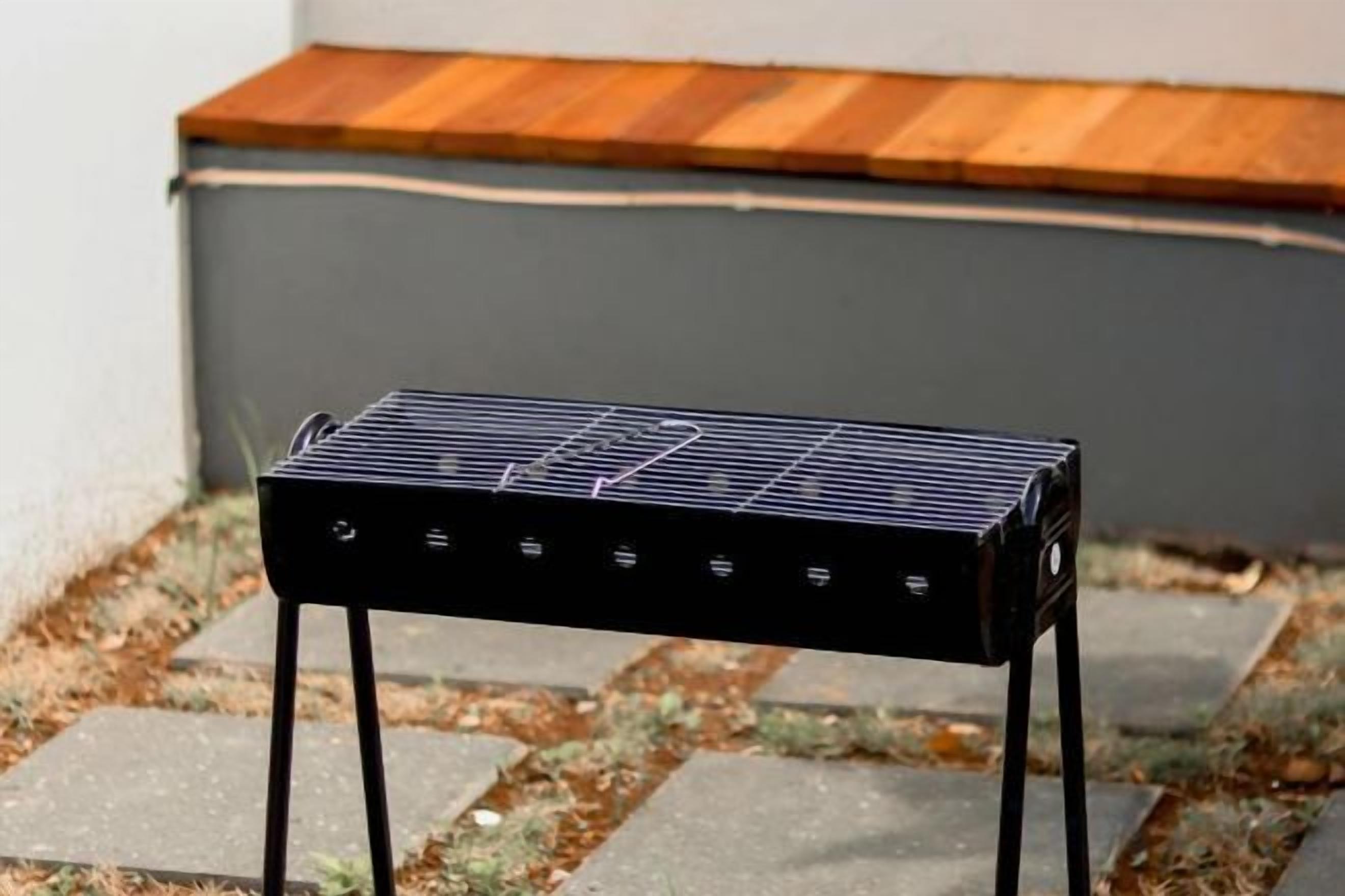 A black barbecue grill with four legs on a paved surface.