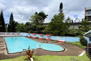Ein Schwimmbecken mit Pflasterrand, umgeben von viel Grün und einem Gebäude im Hintergrund.