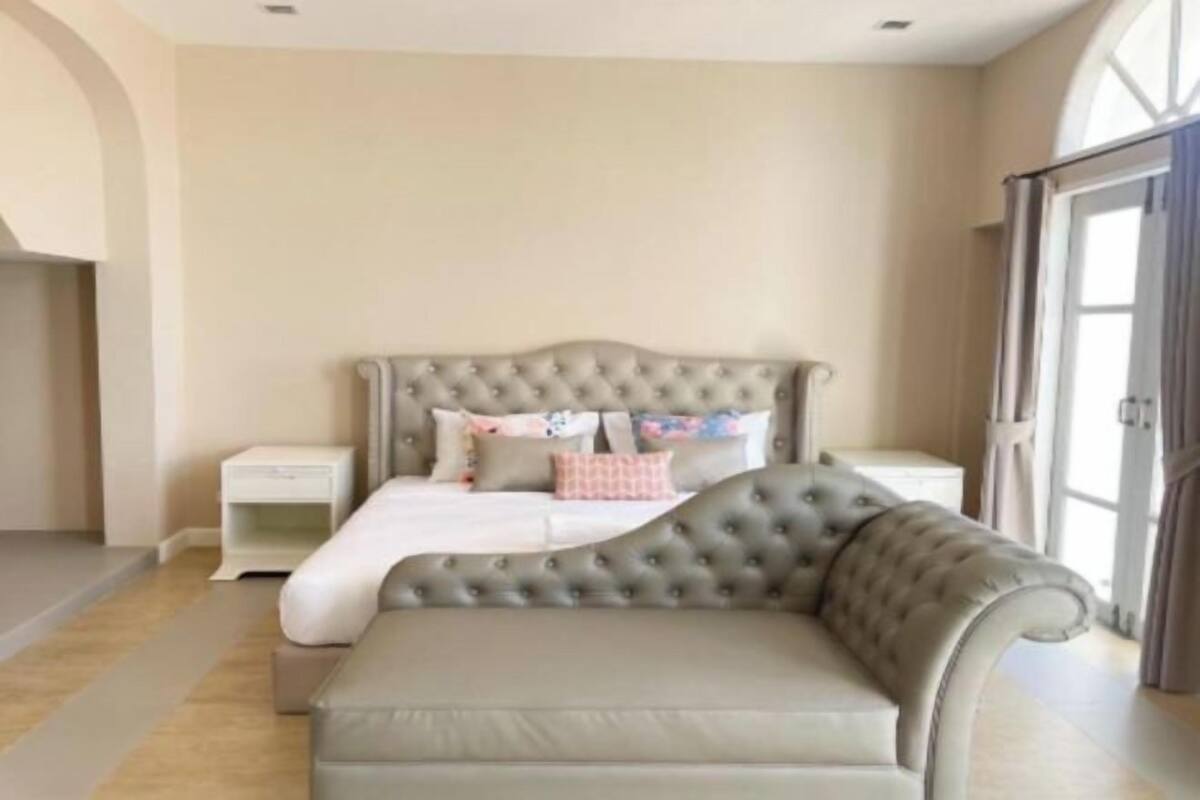 A bedroom with a tufted headboard bed, a grey sofa, and a nightstand.