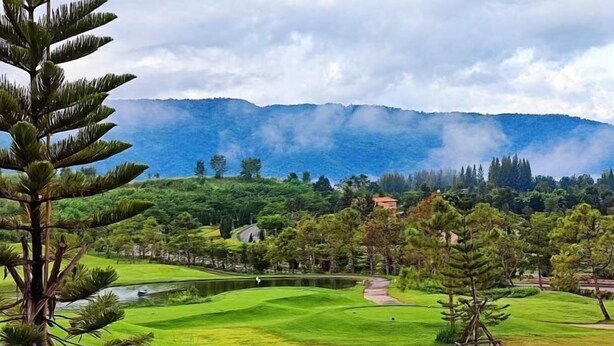 Ein Golfplatz mit Teich, Bäumen und Bergen im Hintergrund.
