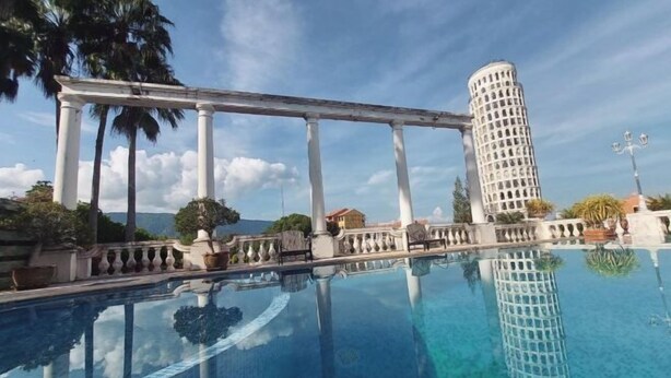 Piscina azul cristalina que refleja un edificio alto y palmeras.