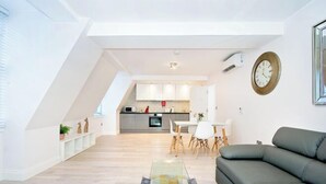 Una sala de estar moderna con un sofá modular, una mesa de centro de vidrio y un comedor con una mesa y sillas blancas.