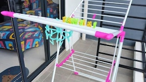 A white and pink drying rack with multiple clips, positioned in front of a colorful, cartoon-themed couch. - LittleChing @ Armadale Residence Galacity (Kuching)