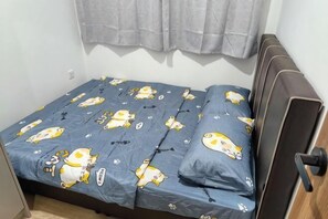 A small, single-bed room with a blue bedspread featuring cartoon characters, a wooden headboard, and a window with curtains. - LittleChing @ Armadale Residence Galacity (Kuching)