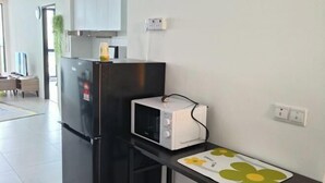 A kitchen with a black refrigerator, a white microwave, and a small table with a flower-patterned placemat. - LittleChing @ Armadale Residence Galacity (Kuching)