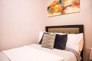 Un letto rifatto con un comofort bianco e diversi cuscini, una testiera e una parete decorata con un'opera d'arte.