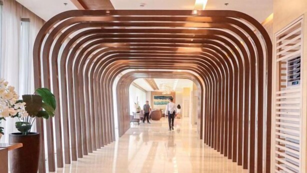 A modern hotel lobby with a curved wooden reception desk, a large potted plant, and a polished marble floor. - Shore 3 Residences Tower 2, Lap Pool and Amenities (Pasay)