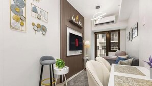 A modern living room with a TV, a sofa, a dining table, and a small side table with a plant. - Shore 3 Residences Tower 2, Lap Pool and Amenities (Pasay)