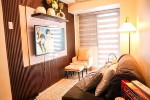 Un soggiorno con una TV a schermo piatto montata a parete, un divano, una poltrona e una lampada.