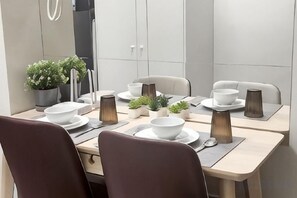 A dining area with a table set for four, including plates, bowls, and cutlery. There are chairs around the table, and a potted plant is visible on the left. - Shore 3 Residences Tower 2, Lap Pool and Amenities (Pasay)