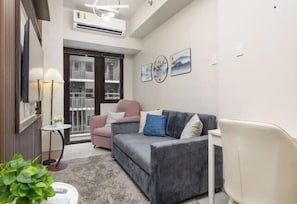 A modern living room with a grey sofa, a pink armchair, a white chair, a small table with a lamp, and a potted plant. - Shore 3 Residences Tower 2, Lap Pool and Amenities (Pasay)