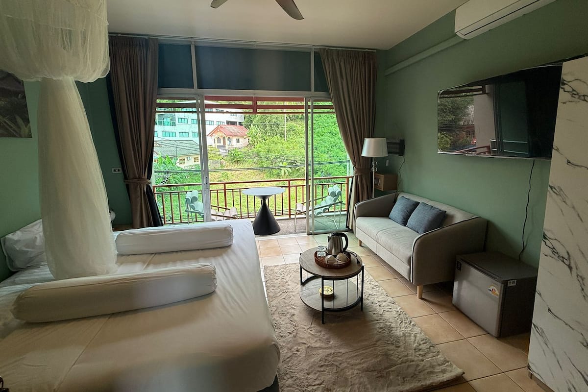 Une chambre d’hôtel avec un lit, un canapé, une petite table, un ventilateur de plafond et une vue sur l’extérieur.