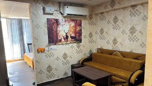 A room with a sofa, a small table, a painting of deer, and an air conditioning unit on the wall. - Golden Punjabi House (Zirakpur)