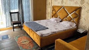 A bedroom with a bed, a chair, a nightstand, and a patterned rug. - Golden Punjabi House (Zirakpur)