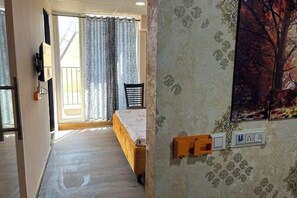 A bedroom with a bed, a chair, a window with curtains, and a wall-mounted electrical outlet. - Golden Punjabi House (Zirakpur)