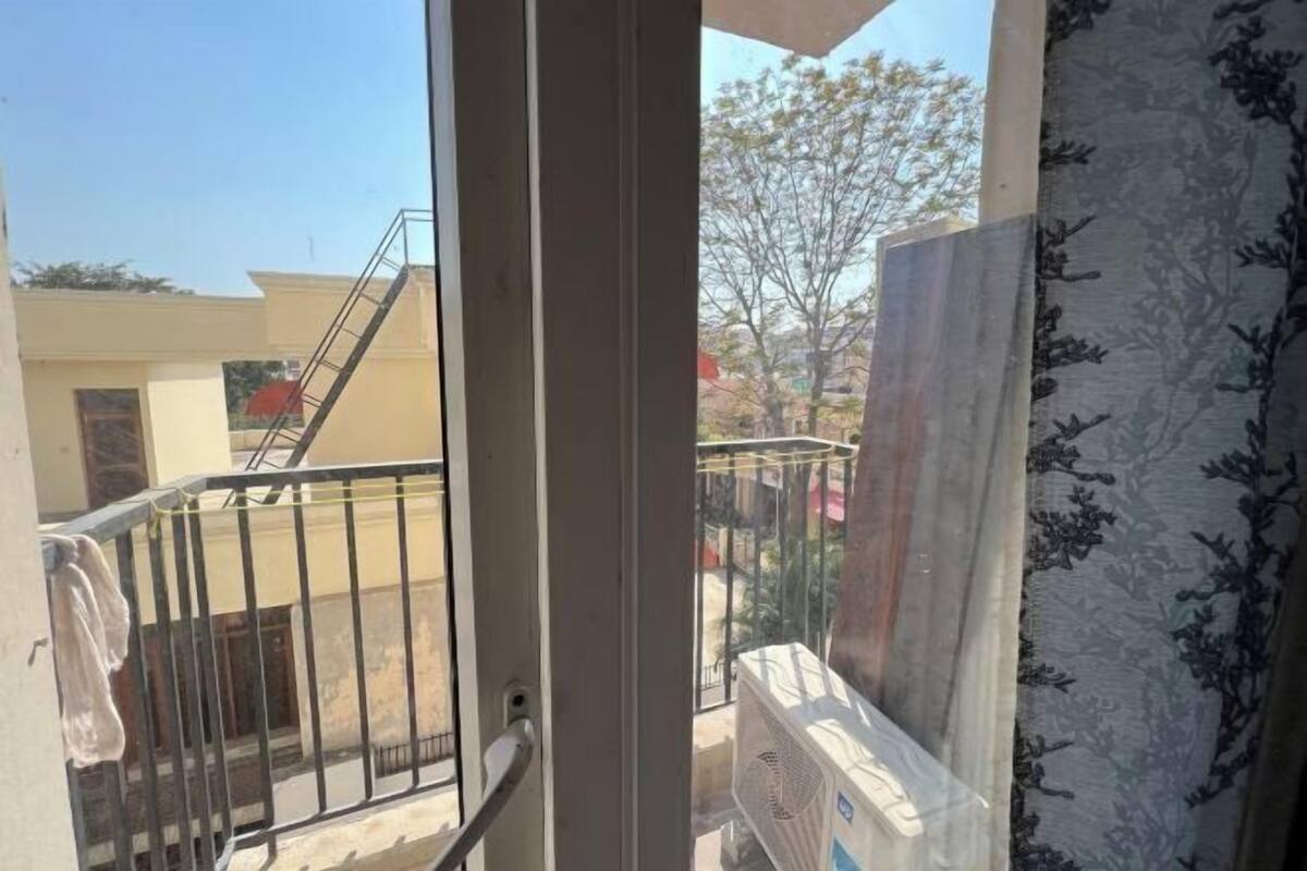 A balcony with a metal railing, a view of a neighboring building, and a large air conditioning unit.