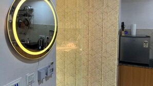 A bathroom with a round mirror, a shower area, and a kitchen counter. - Golden Punjabi House (Zirakpur)