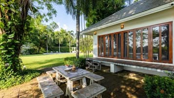 Un'area pranzo all'aperto coperta, con tavoli e panche, immersa nel verde e con vista su un prato.