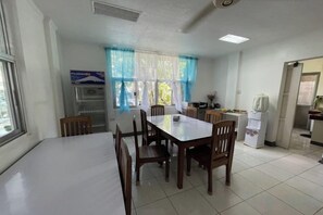 Un comedor con una mesa, sillas, un refrigerador y una ventana con cortinas.