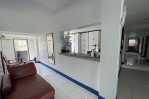 A hotel lobby with a reception desk, a waiting area with a brown sofa, and a hallway leading to other rooms.