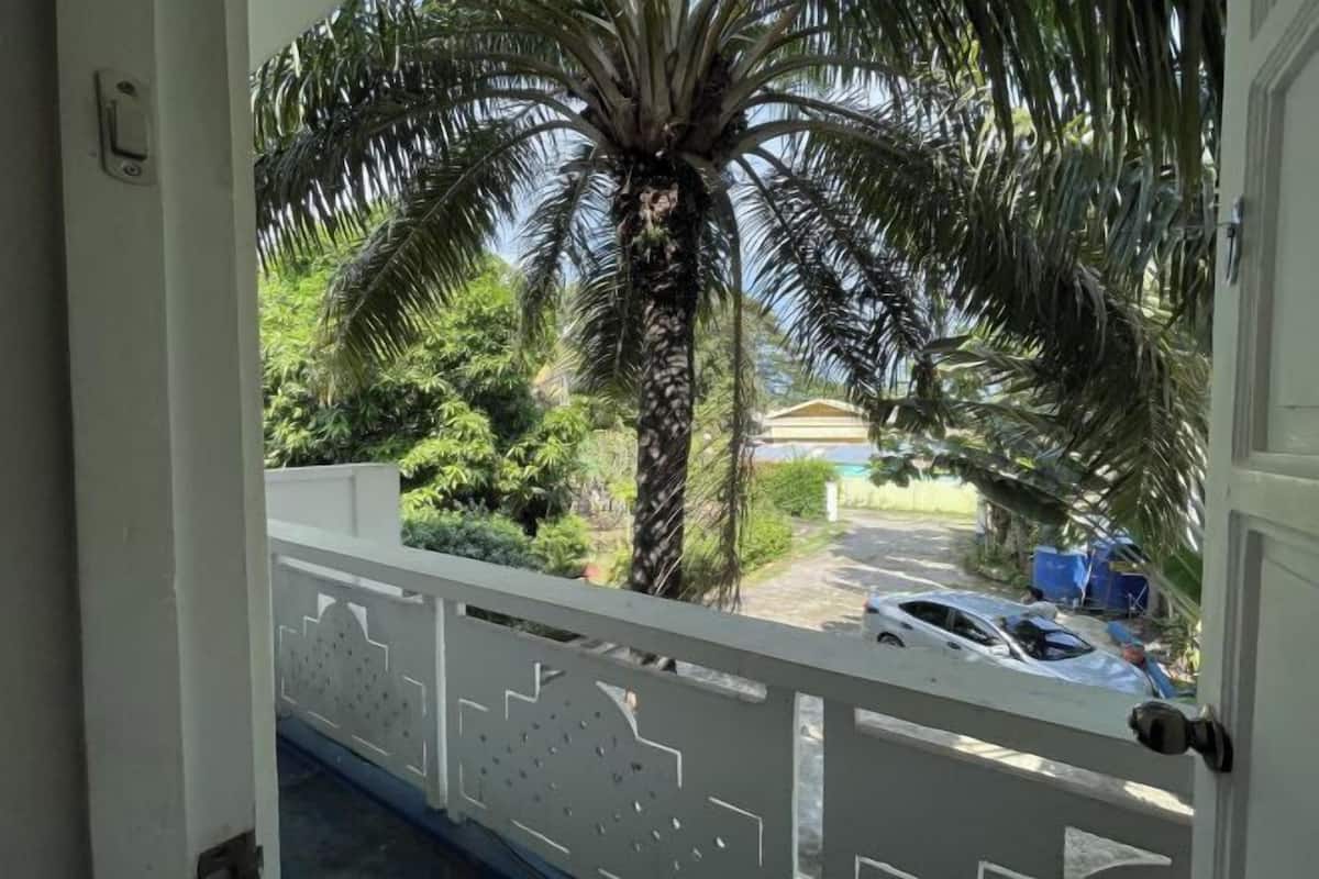 Un balcon avec une balustrade blanche, un palmier et une voiture garée en arrière-plan.