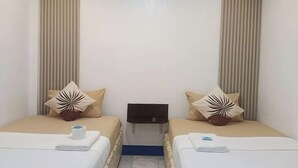 Hotelkamer met twee bedden, beige beddengoed, decoratieve kussens, een klein tafeltje en een vastgemaakt hoofdbord.