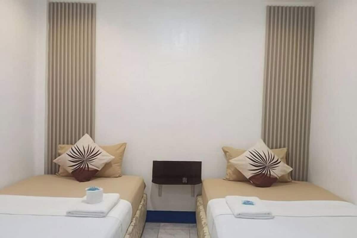 Une chambre d’hôtel avec deux lits, une literie de couleur beige, des coussins décoratifs, une petite table et une tête de lit fixée au mur.