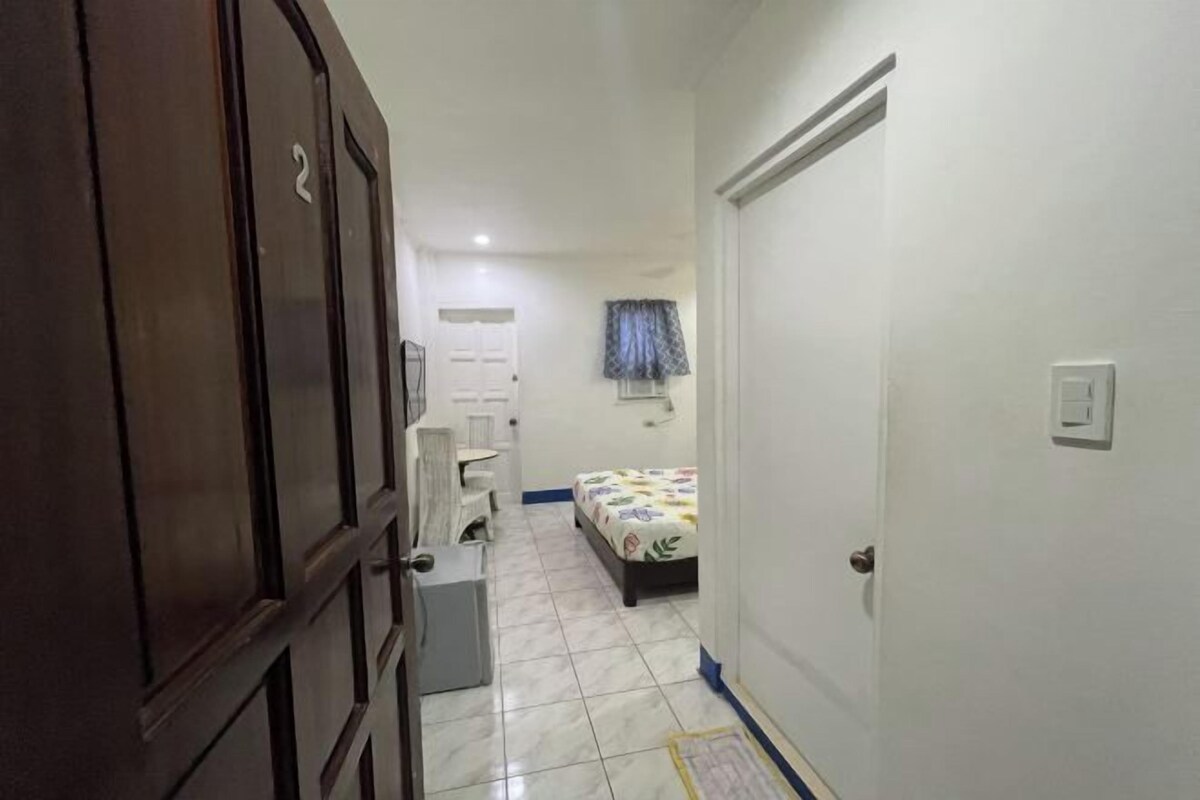 Un pasillo estrecho que conduce a un dormitorio con una cama, un escritorio pequeño y una silla.