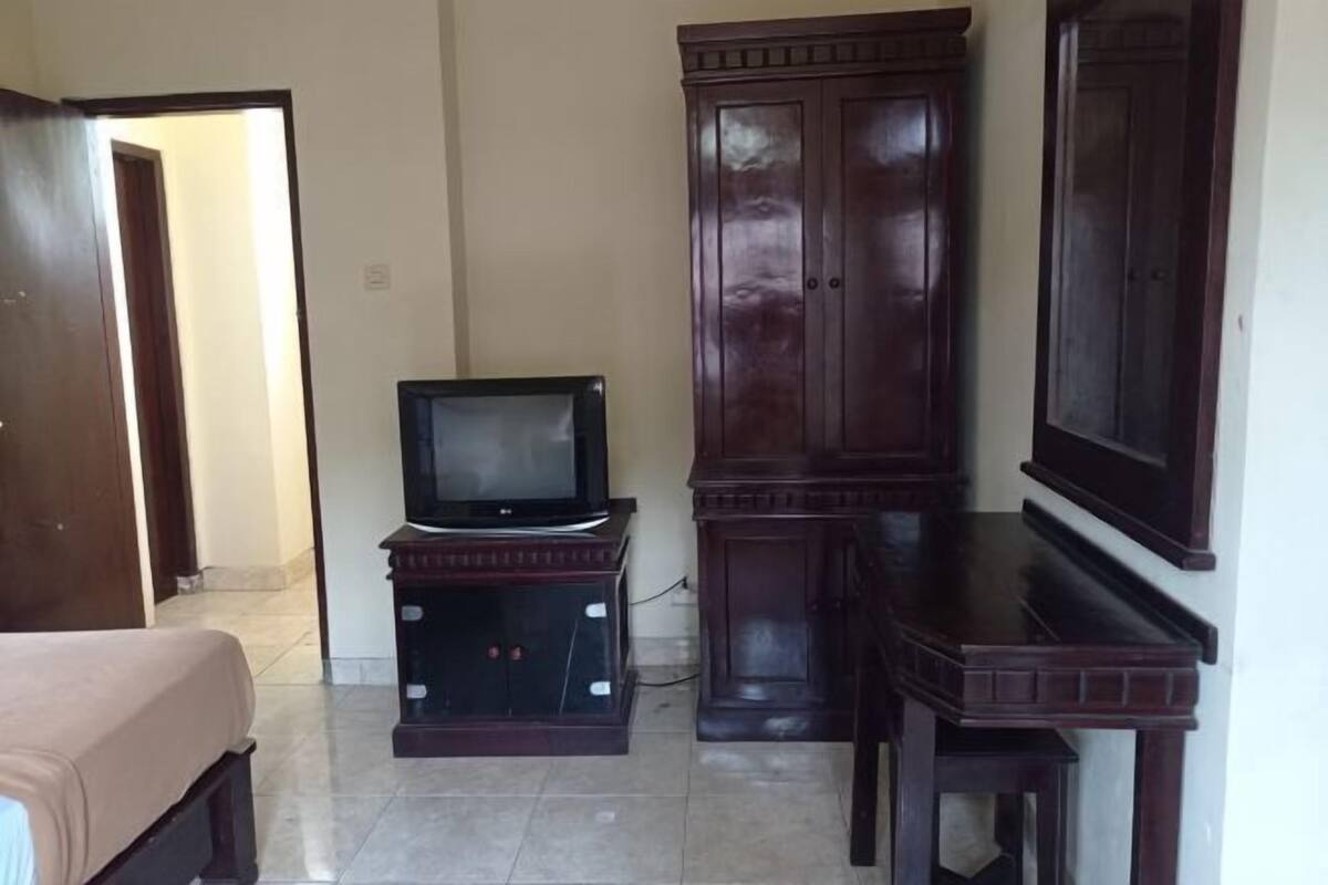 A room with a bed, a television on a stand, a wardrobe, and a cabinet.