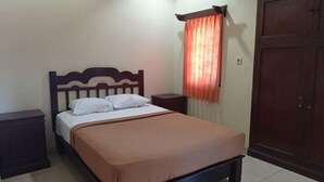 A single bed with a wooden headboard, a nightstand, a wardrobe, and a window with a curtain. - Hotel Mawar Sari Mitra RedDoorz (Bali)