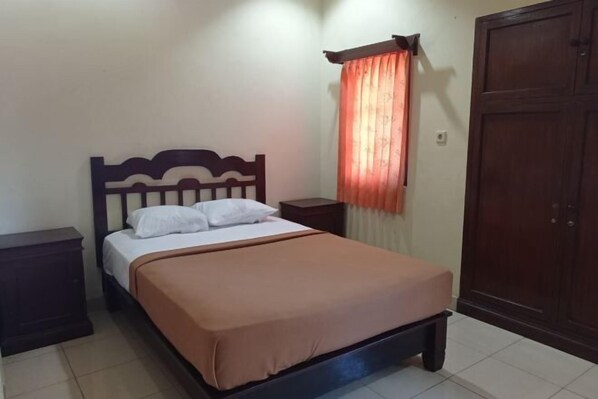 A single bed with a wooden headboard, a nightstand, a wardrobe, and a window with a curtain. - Hotel Mawar Sari Mitra RedDoorz (Bali)