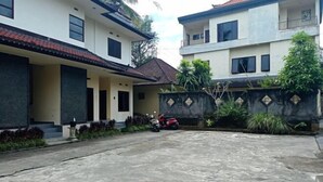 A residential area with two-story houses, a concrete driveway, and a parked motorcycle. - Hotel Mawar Sari Mitra RedDoorz (Bali)