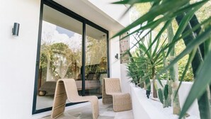 A modern outdoor patio with two wicker chairs, a glass door leading to a garden, and a white wall with a small plant. - X Villa Khana · Exquisite 3br villa Canggu (Bali)