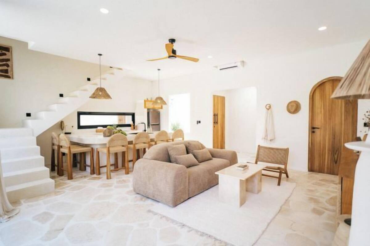 A spacious living area with a sofa, dining table, and chairs, a staircase, and a ceiling fan.