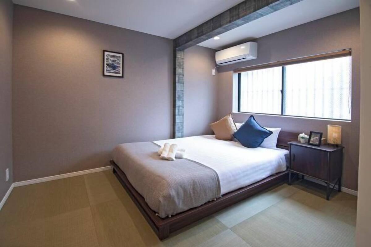 Une chambre à coucher comprenant un lit, une table de chevet, une fenêtre et un appareil de climatisation.